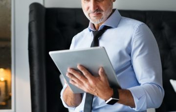 mature-businessman-with-tablet-in-a-hotel-room–e1624415796363 mature-businessman-with-tablet-in-a-hotel-room--e1624415796363